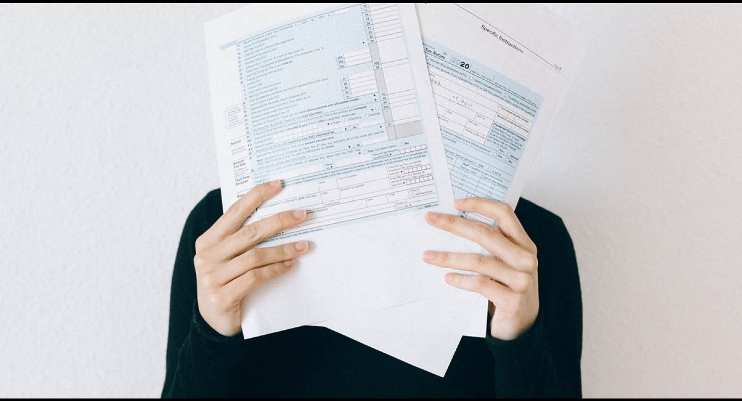 Visage d'étudiante caché derrière une panoplie de formulaires d'impôt