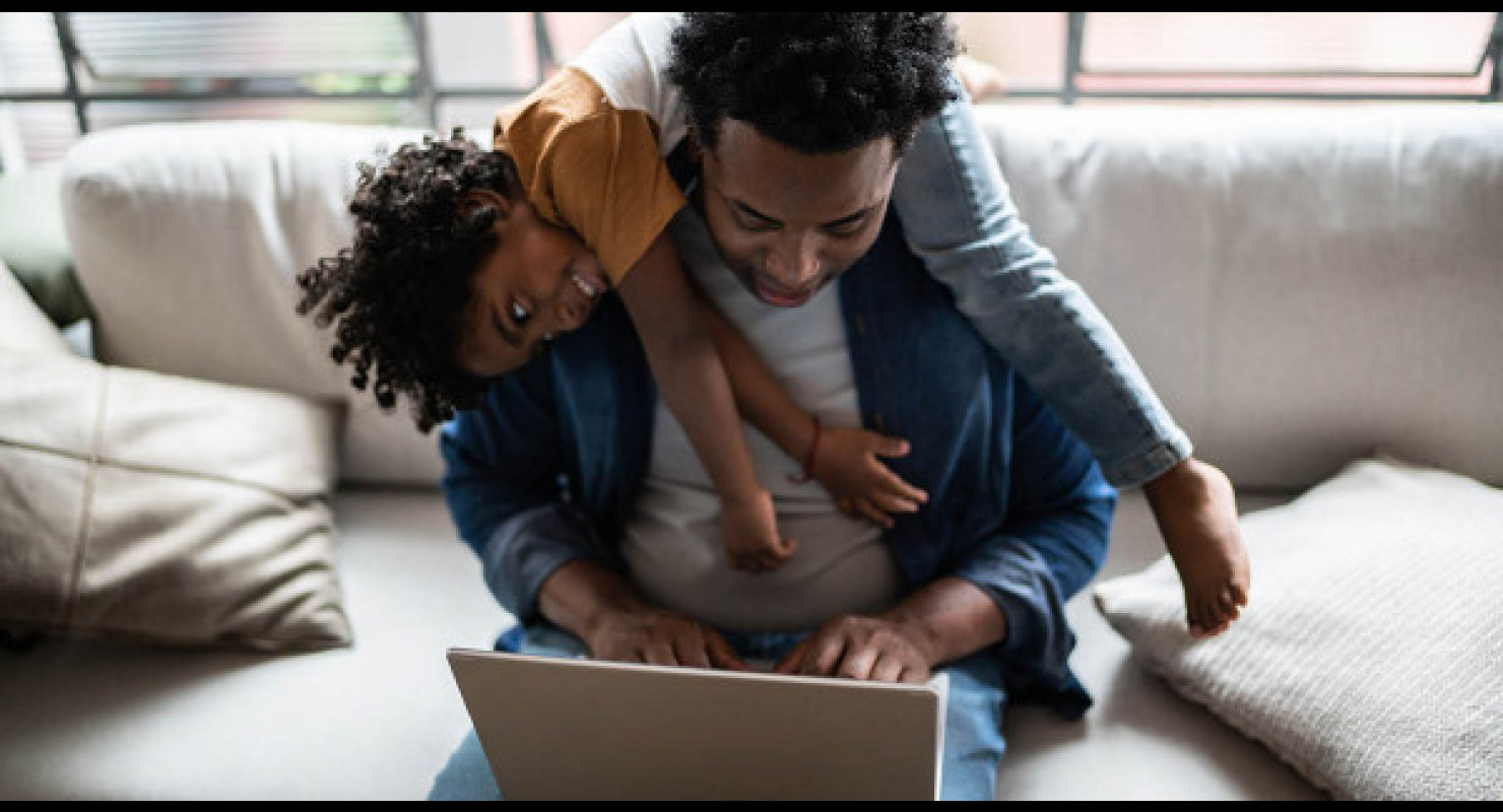 Un jeune papa en train de travailler sur son ordinateur portable avec un enfant sur ses épaules