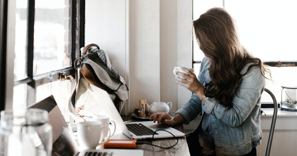 Étudiante assise devant son ordinateur portable en train de boire un café