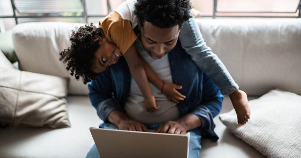 Un jeune papa en train de travailler sur son ordinateur portable avec un enfant sur ses épaules