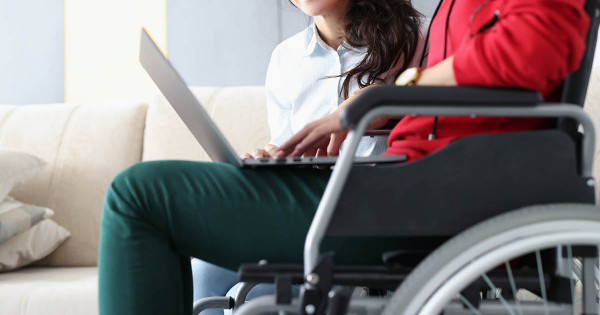 Étudiante en situation de handicap physique assise sur une chaise roulante en train d'étudier à son ordinateur portable