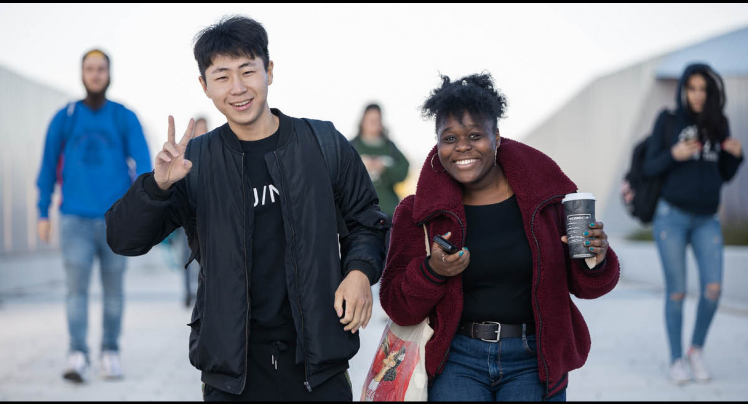 Une étudiante et un étudiant issus de la diversité souriant et marchant dehors au campus MIL